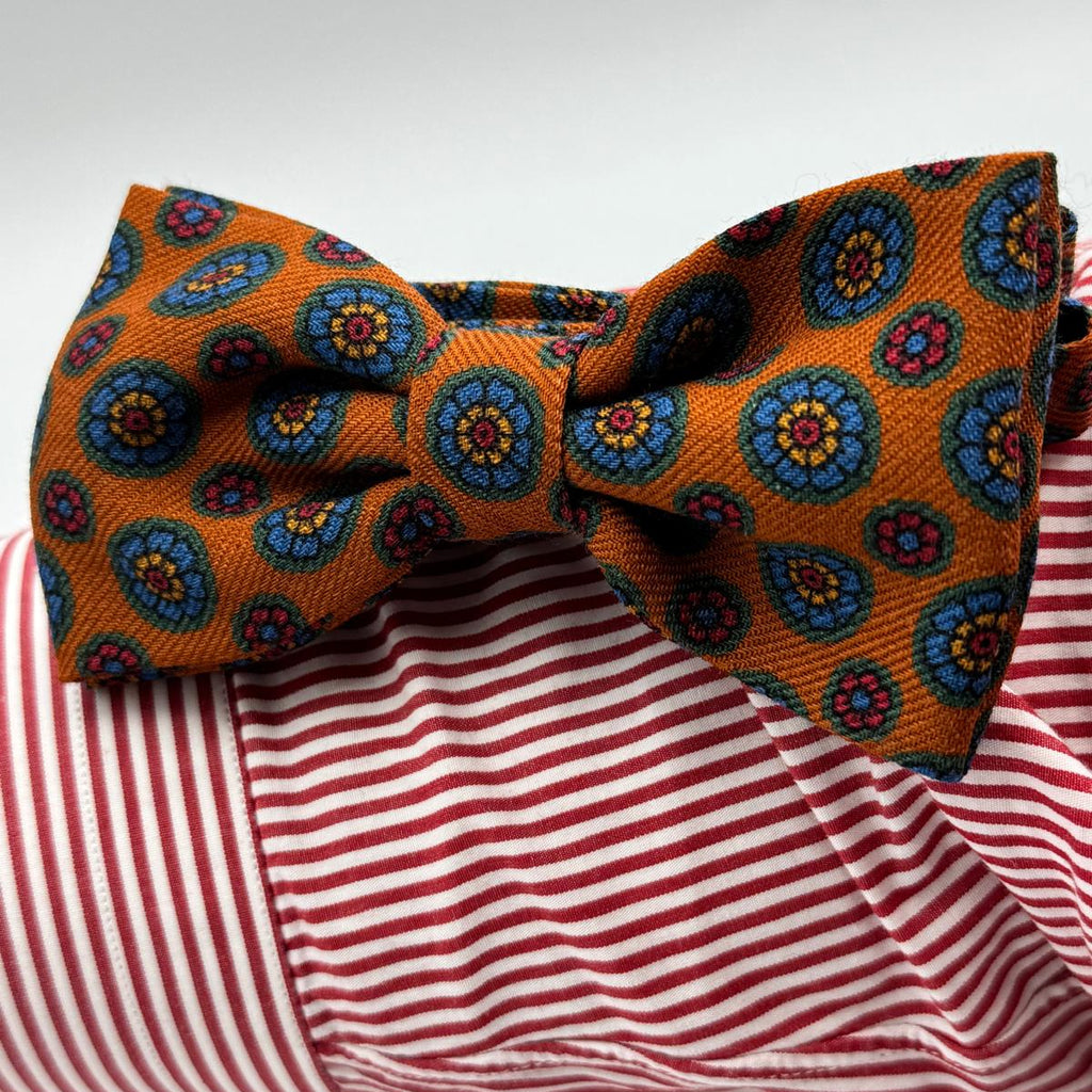 Cruciani &amp; Bella Bow Tie
85% Silk and 15 % Wool Made in England
Handmade in Italy
Rust, Red, Orange, Light Blue and Yellow motif
Coated metal Labels
Bow Ties